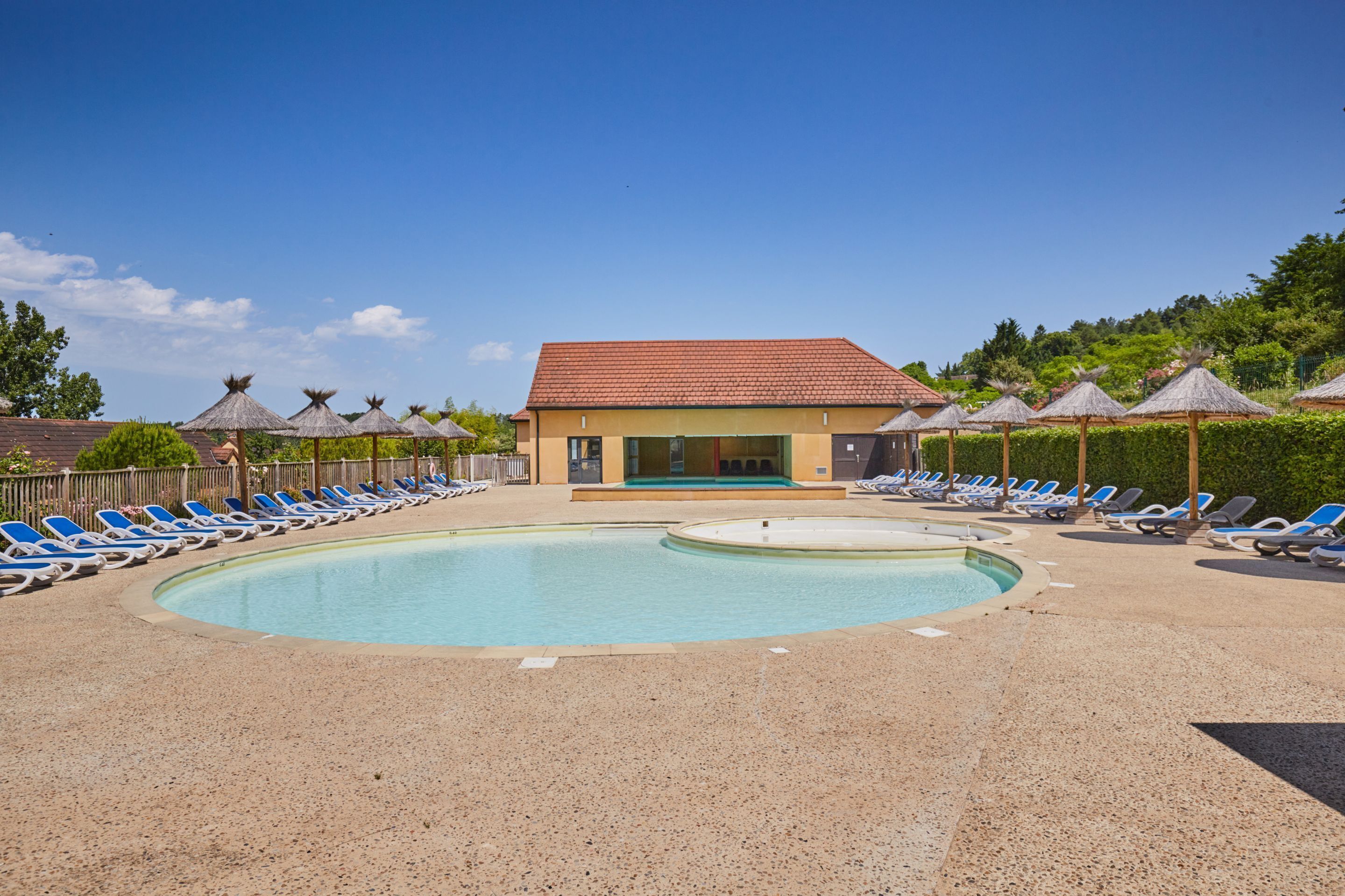 A pool area with lounge chairs and a building with a red roof.
