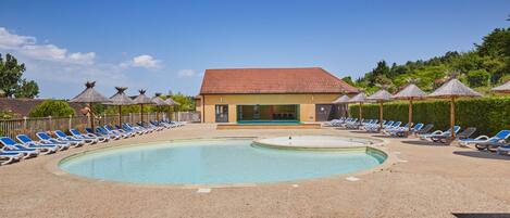 A pool area with lounge chairs and a building with a red roof.