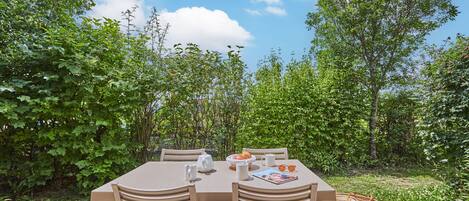 An outdoor dining area with a table and chairs, surrounded by greenery.