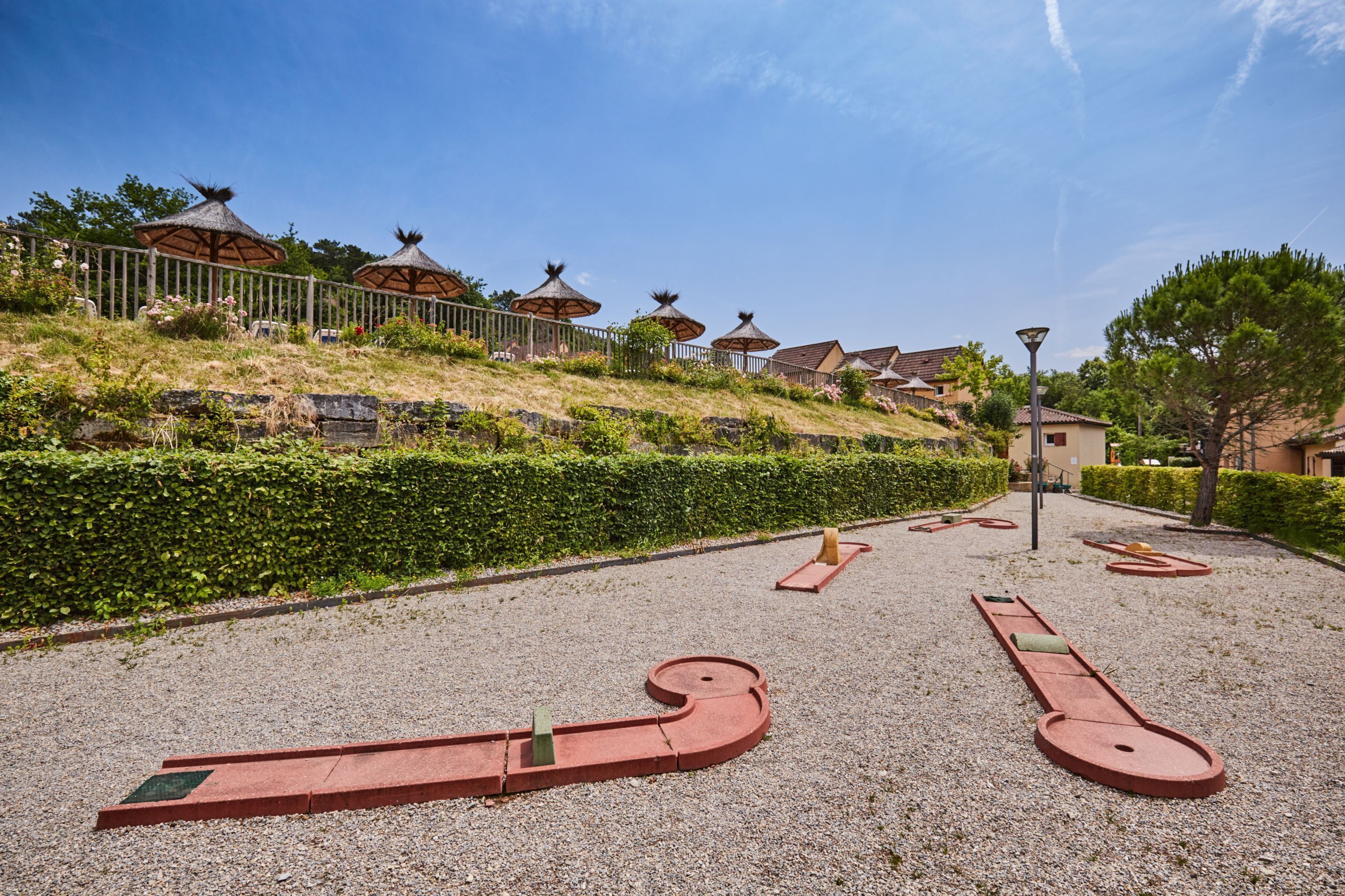 Un área pavimentada con formas geométricas y una cerca con construcciones de techo de paja al fondo.