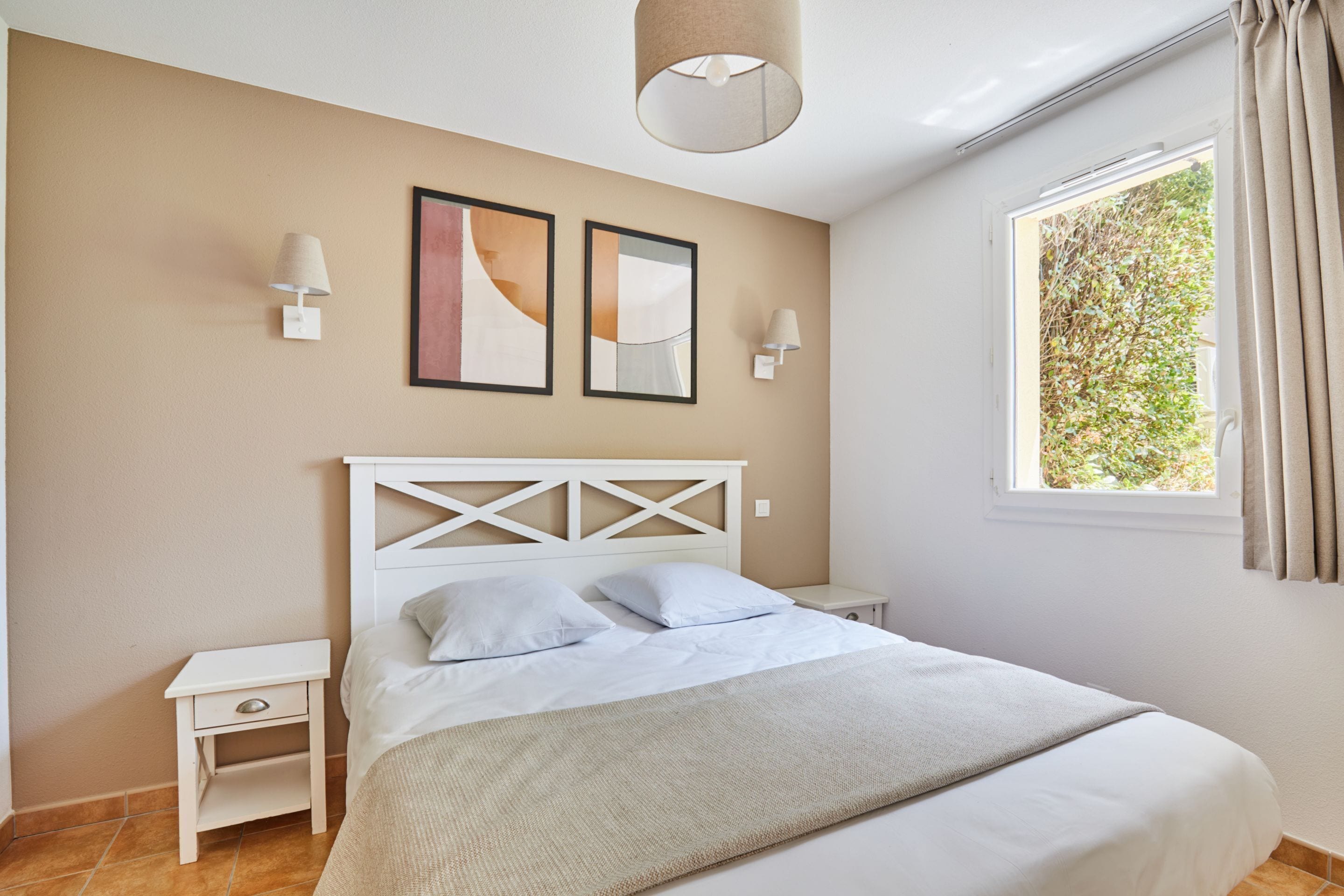 Une chambre à coucher comprenant un lit, des tables de chevet, des lampes fixées au mur et des œuvres d’art encadrées.