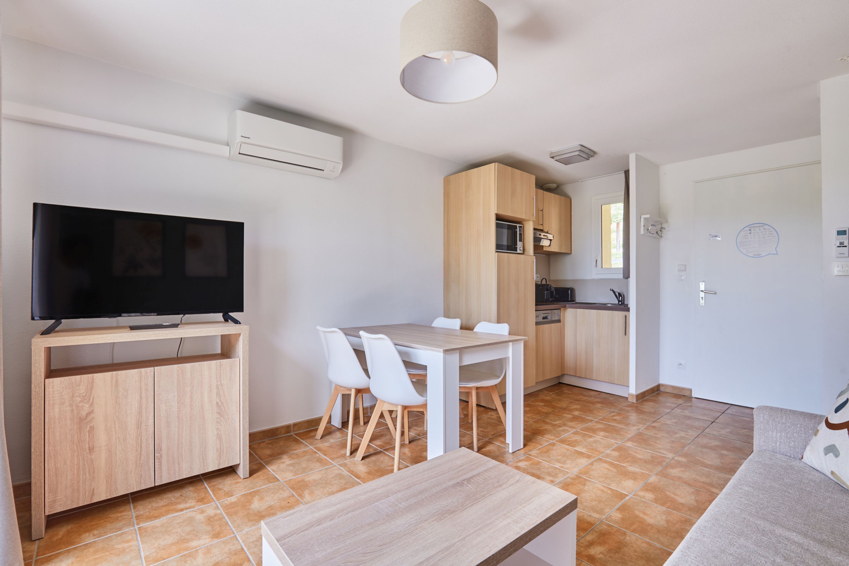 Una cocina moderna con armarios de madera, una mesa de comedor con sillas, un televisor sobre un mueble de madera y una lámpara en el techo.