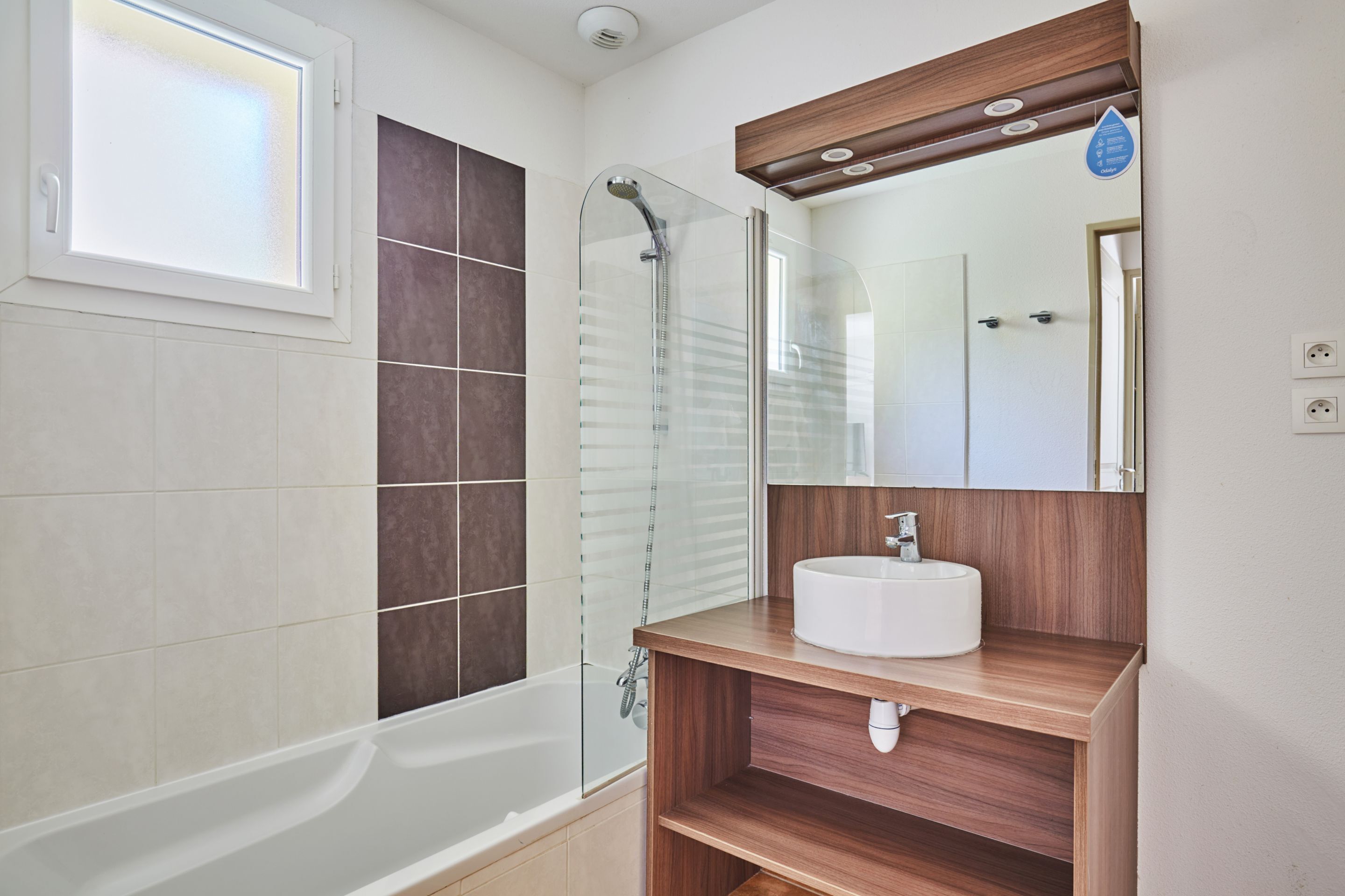 A modern bathroom with a glass shower enclosure, a white bathtub, and a wooden vanity with a white sink.