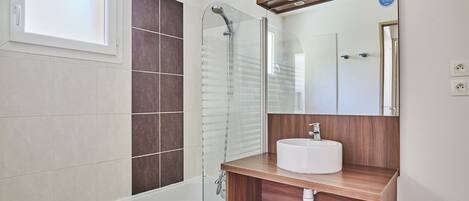 A modern bathroom with a glass shower enclosure, a white bathtub, and a wooden vanity with a white sink.