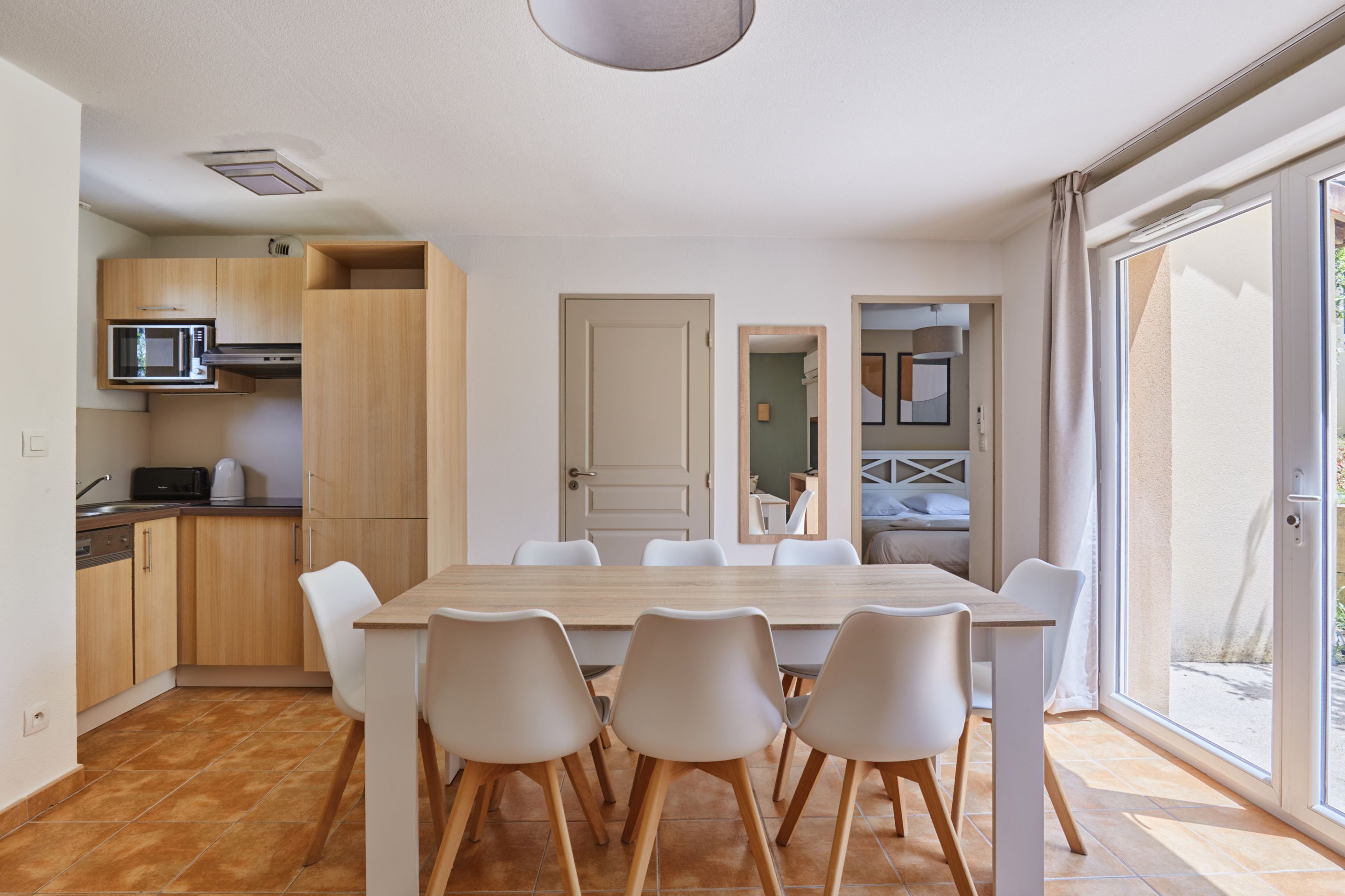 A modern kitchen with a dining area, wooden cabinets, a microwave, and a large window.