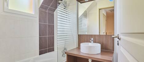 Un baño moderno con bañera, ducha con mampara de vidrio y tocador de madera con lavamanos.