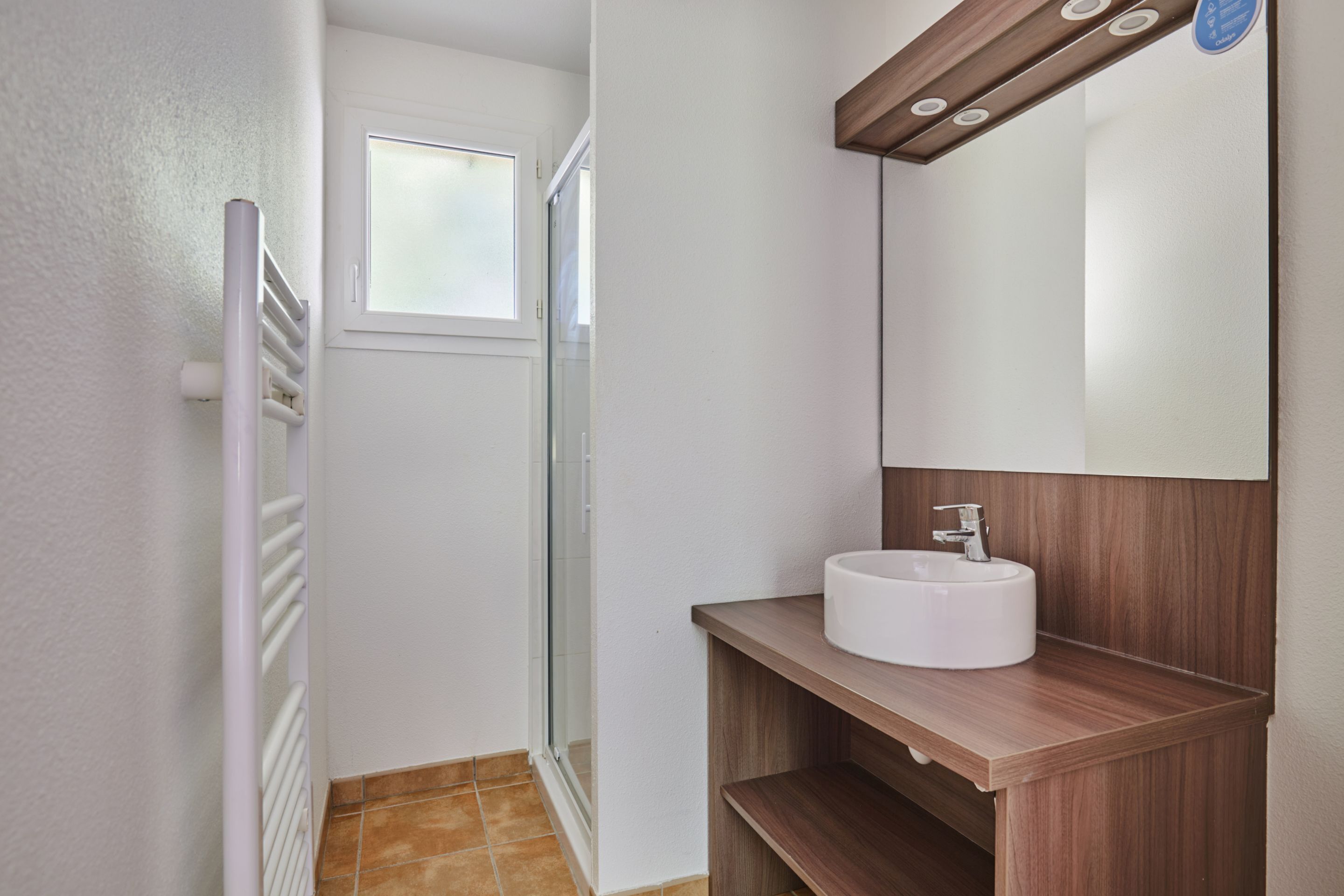 Un baño con lavamanos blanco, tocador de madera y cabina de ducha de vidrio.