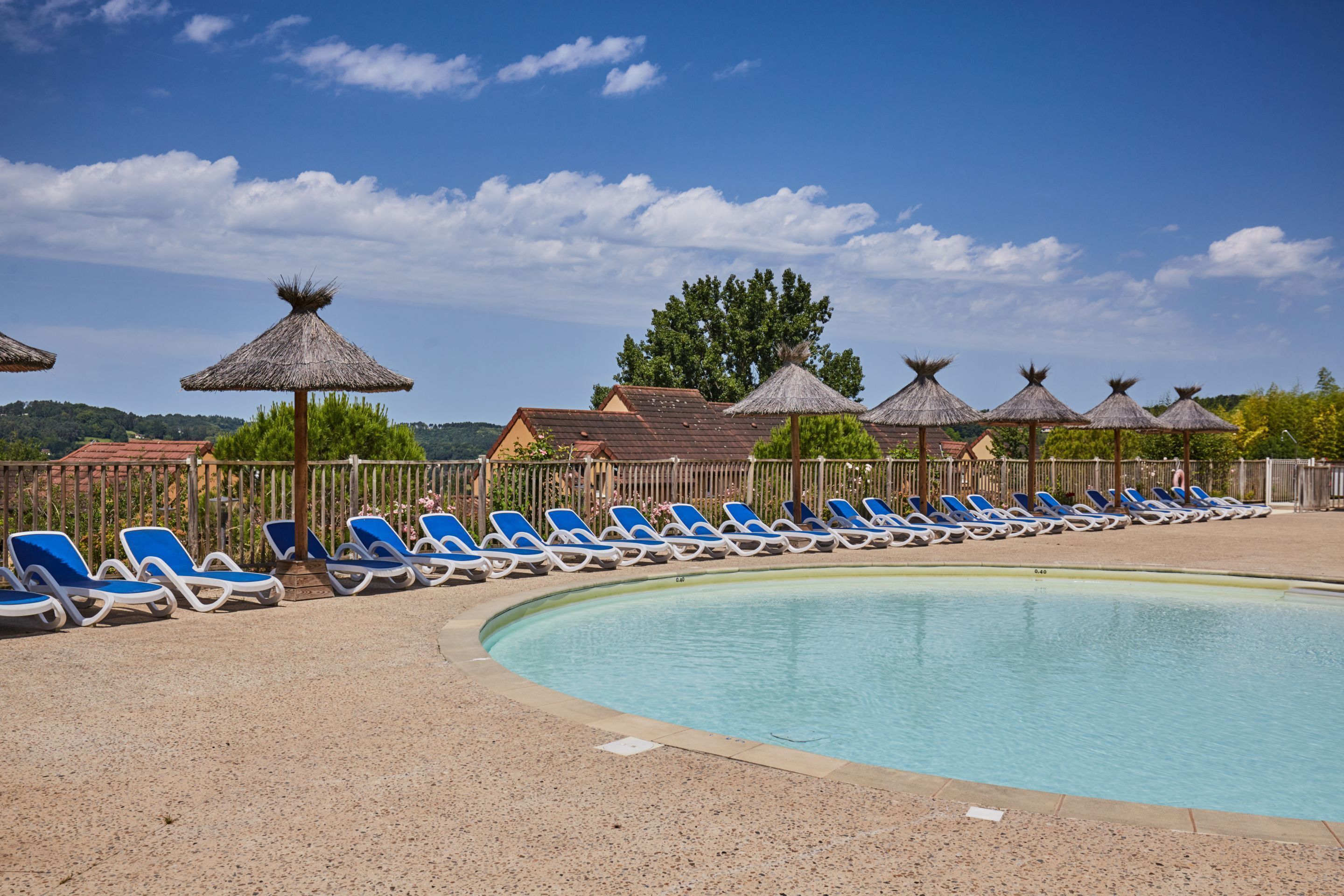 A swimming pool with blue lounge chairs and thatched umbrellas.