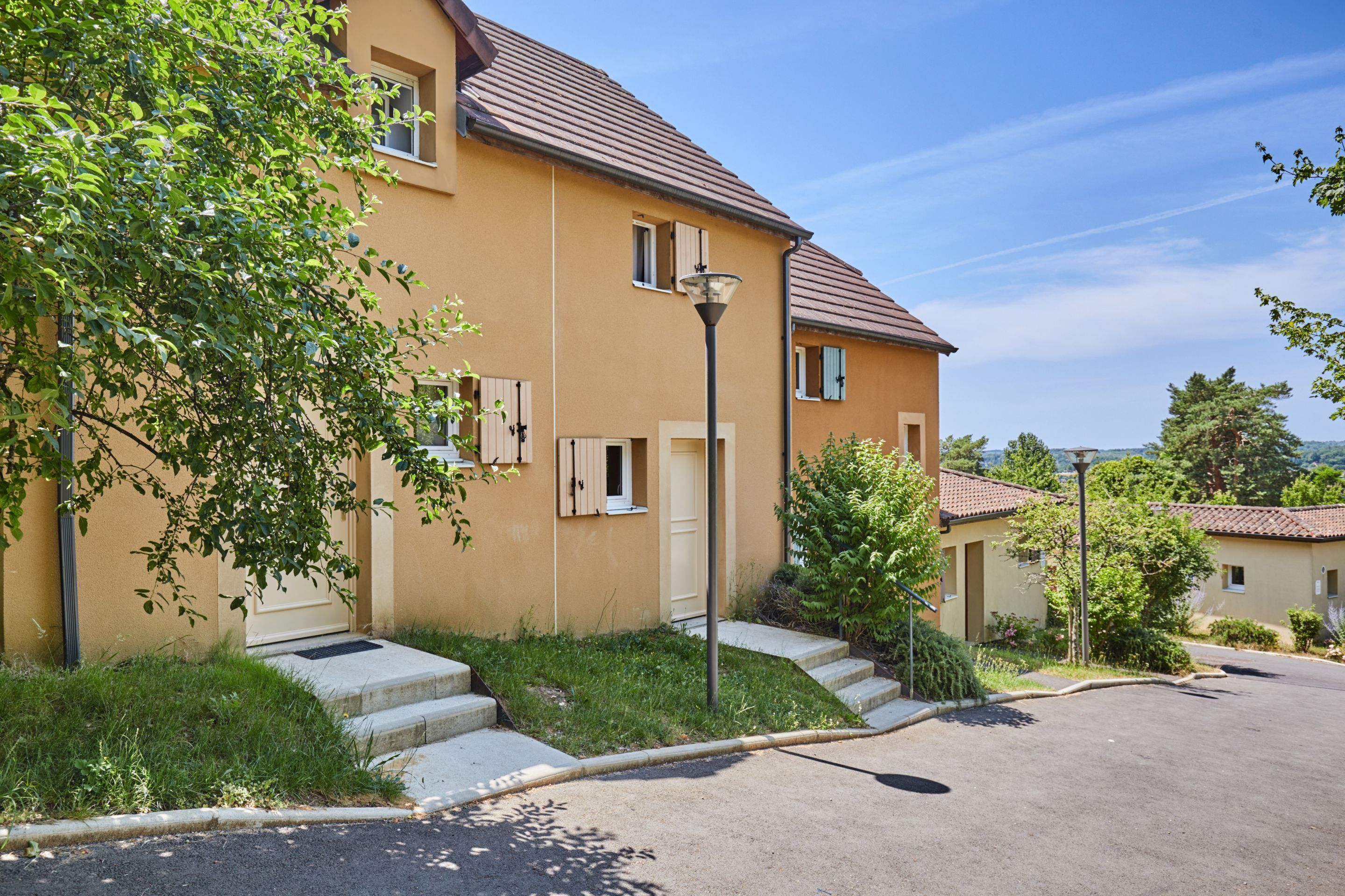 A two-story building with a beige facade, a tiled roof, and a paved driveway.