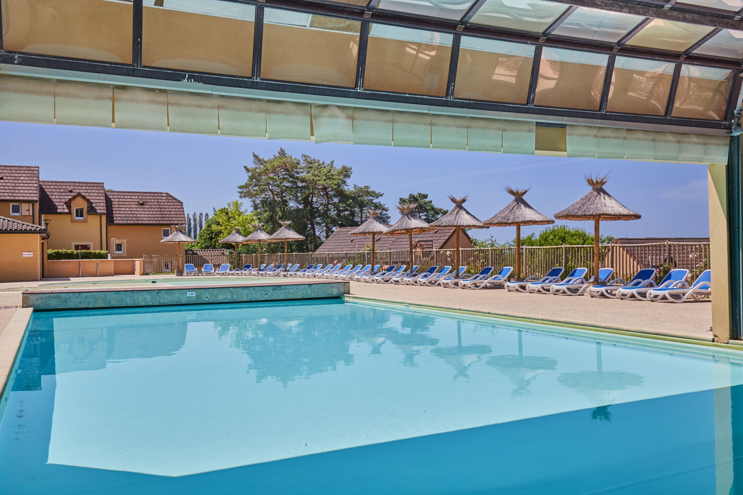 A swimming pool with lounge chairs and umbrellas, surrounded by buildings and trees.