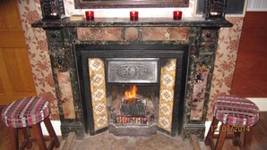 A fireplace with a fire, two stools, and three candles on the mantel. - Beggar's Knap (Dorchester)