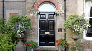 A black double door with a brick archway above it, flanked by two flower boxes with red and purple flowers. - Beggar's Knap (Dorchester)