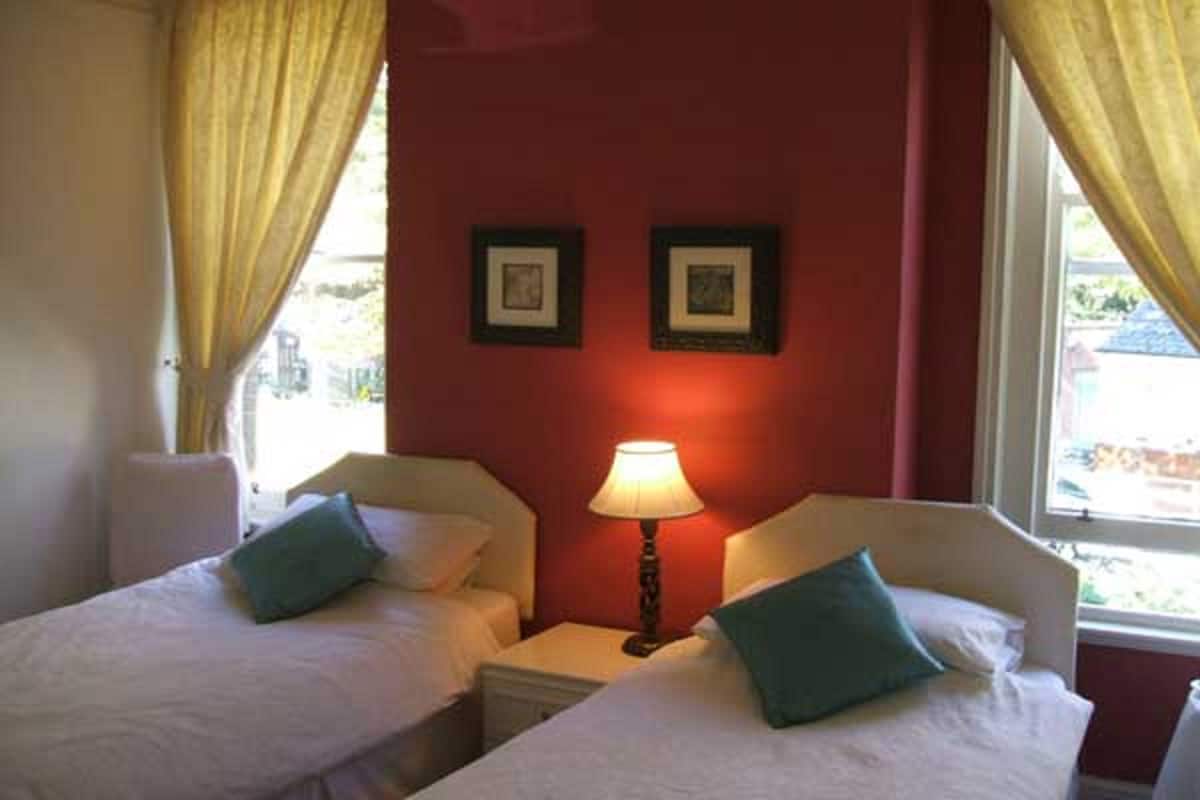Habitación de hotel con dos camas, una mesita de noche con lámpara y dos cuadros enmarcados en la pared.