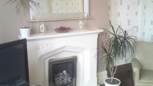 Una sala de estar con chimenea, un espejo encima y dos plantas en macetas.