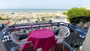 A balcony with a table and chairs, overlooking a beach and a cityscape.