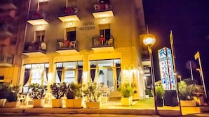 A hotel named "HOTEL RICCARDI" with multiple balconies, large windows, and potted plants in the foreground.