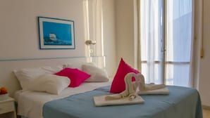 A hotel room with a bed, pillows, a nightstand, a framed picture, and a window with curtains.