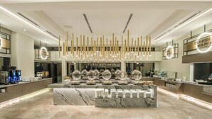 Een moderne hotel lobby met een marmeren receptiebalie, decoratieve verlichtingsarmaturen en een koffieapparaat.