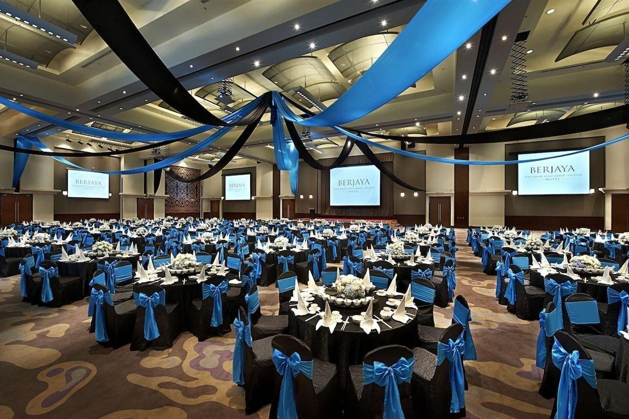 Une grande salle de conférence avec de nombreuses rangées de tables, chacune étant agrémentée d’une chaise bleue et d’un chemin de table blanc.