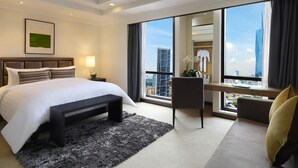 Een moderne hotelkamer met een groot bed, een bureau en uitzicht op de stad door grote ramen.