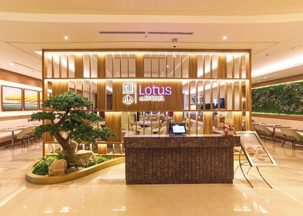 Et moderne Lotus hotel med et træreceptionsskranke, en digital skærm og en stor væg med en grøn plantagemur.