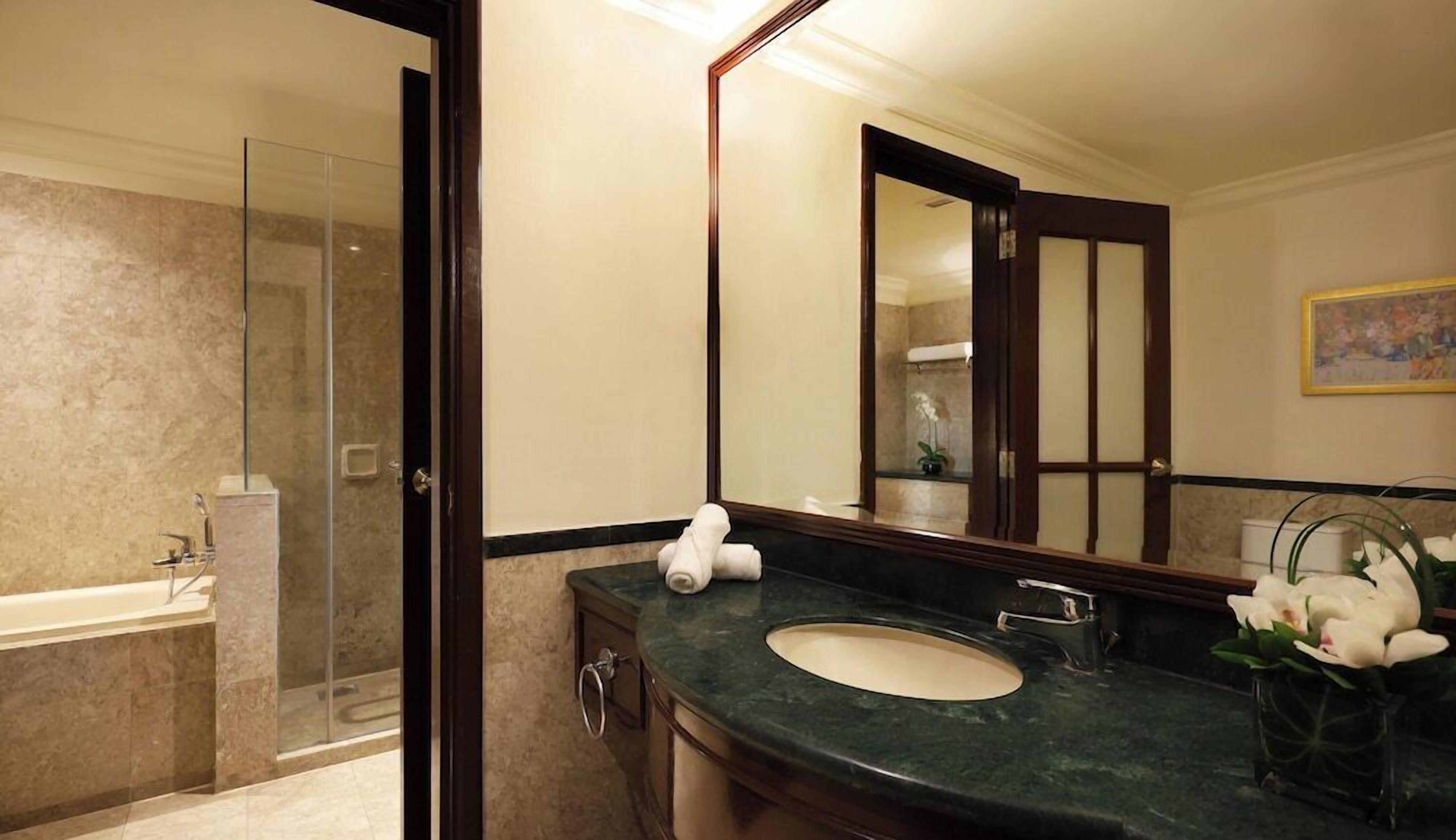 A bathroom with a glass shower, a sink, a mirror, and a vase with flowers.