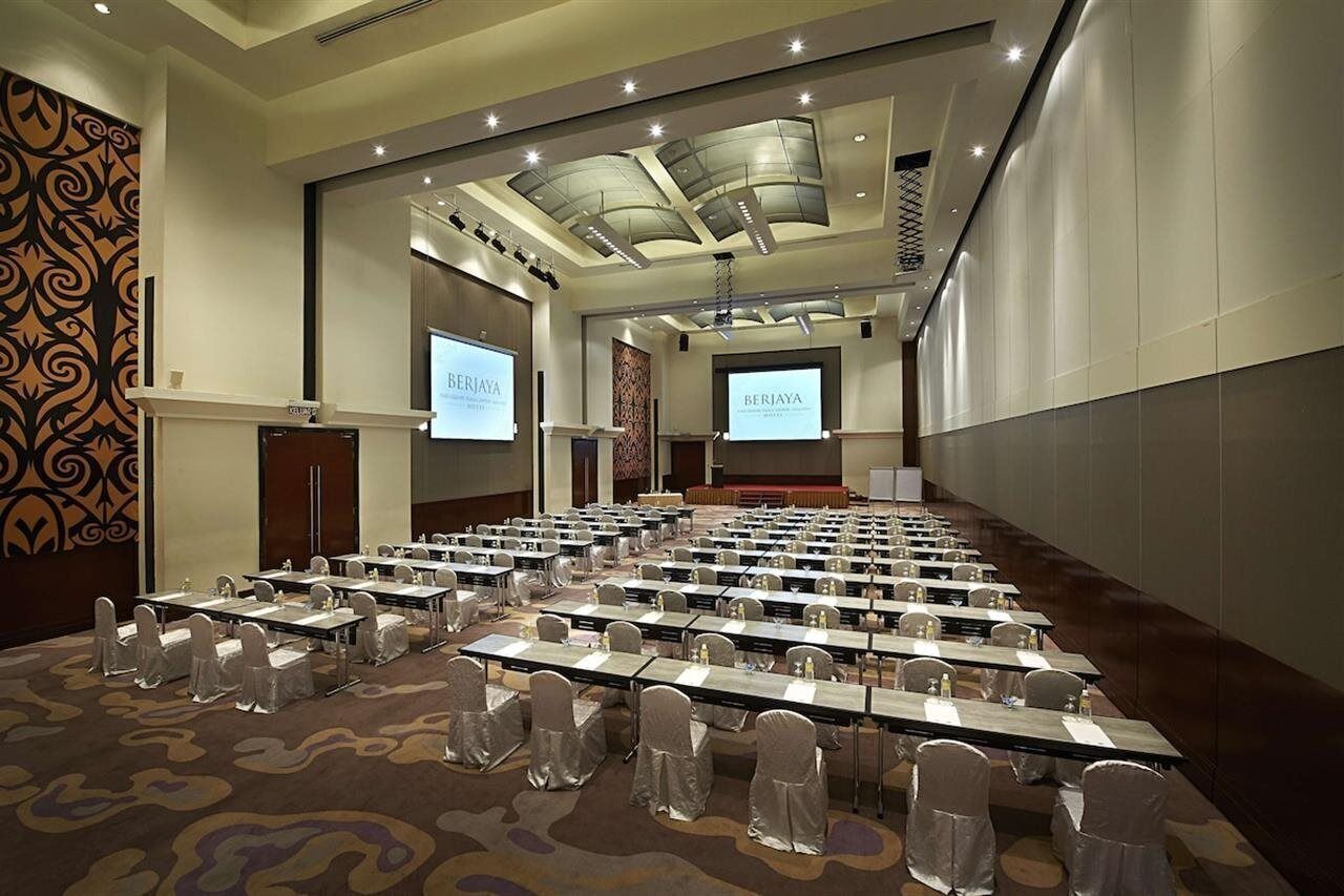 A conference room with rows of tables and chairs, a stage, and presentation screens.