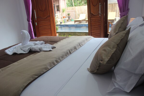 Un dormitorio con cama, almohadas y vistas a una piscina al aire libre.