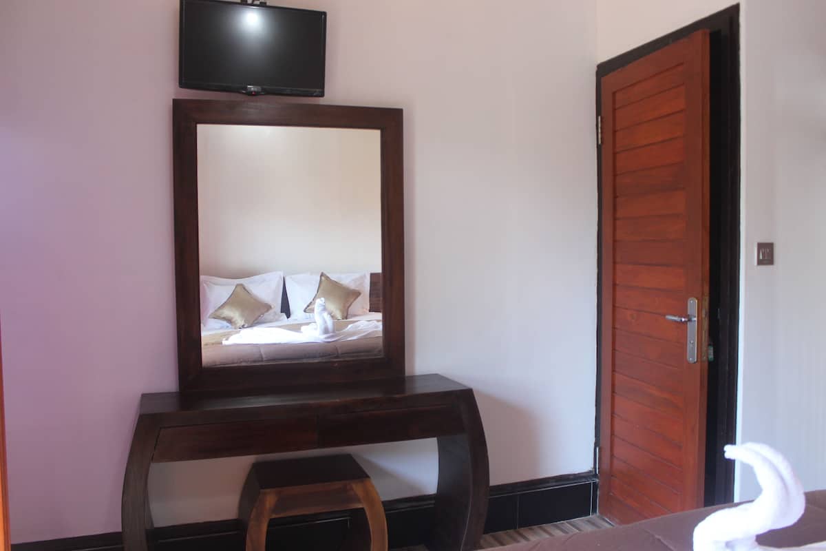 A room with a wooden console table, a mirror, a television mounted above it, and a wooden door.