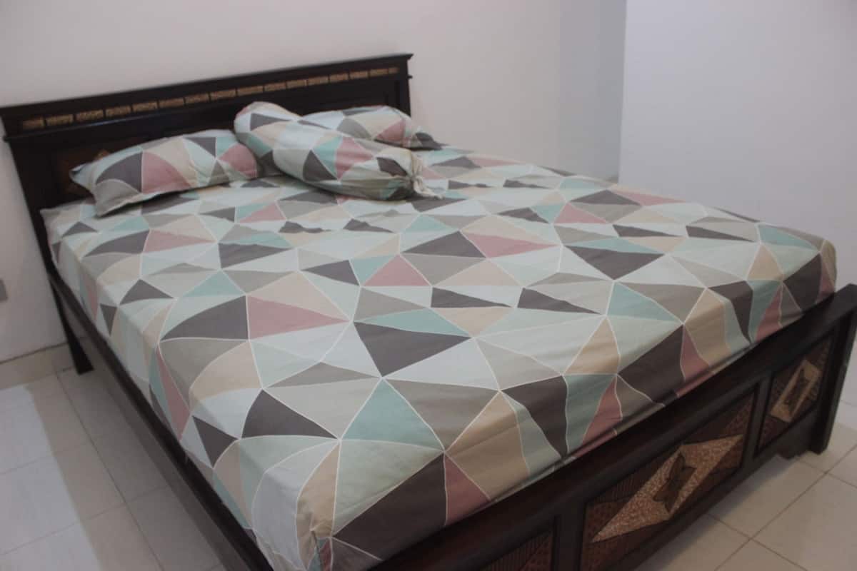 A bed with a geometric patterned bedspread and pillows, a wooden headboard, and a dark wooden frame.