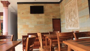 Un comedor con mesas y sillas de madera, un televisor de pantalla plana montado en la pared y un panel decorativo.