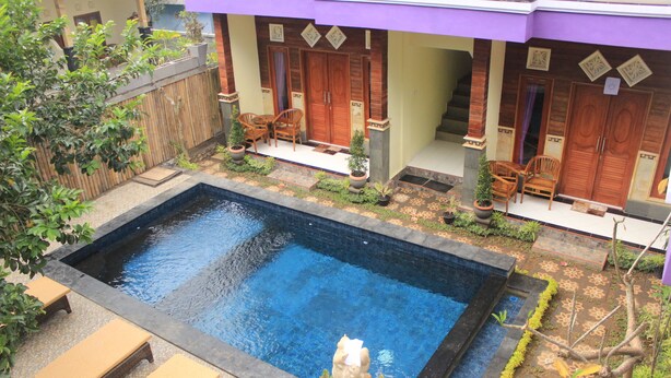 Piscina con una estatua, puertas de madera y un porche cubierto con sillas.
