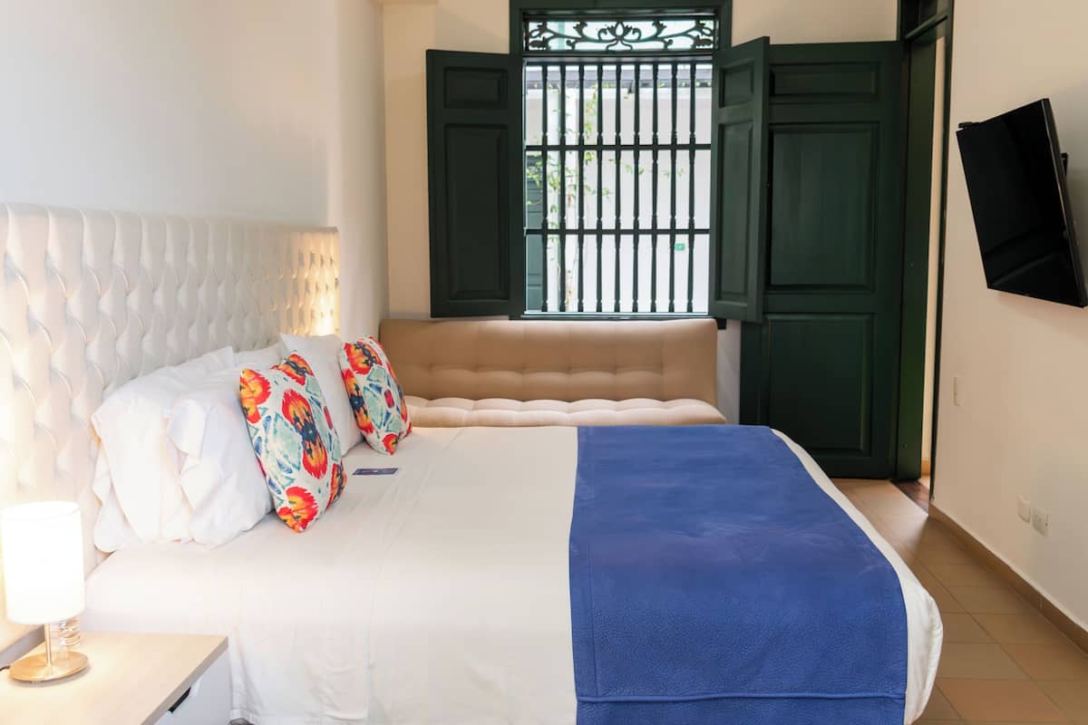 A neatly made bed with a white headboard, a blue blanket, and colorful floral pillows.