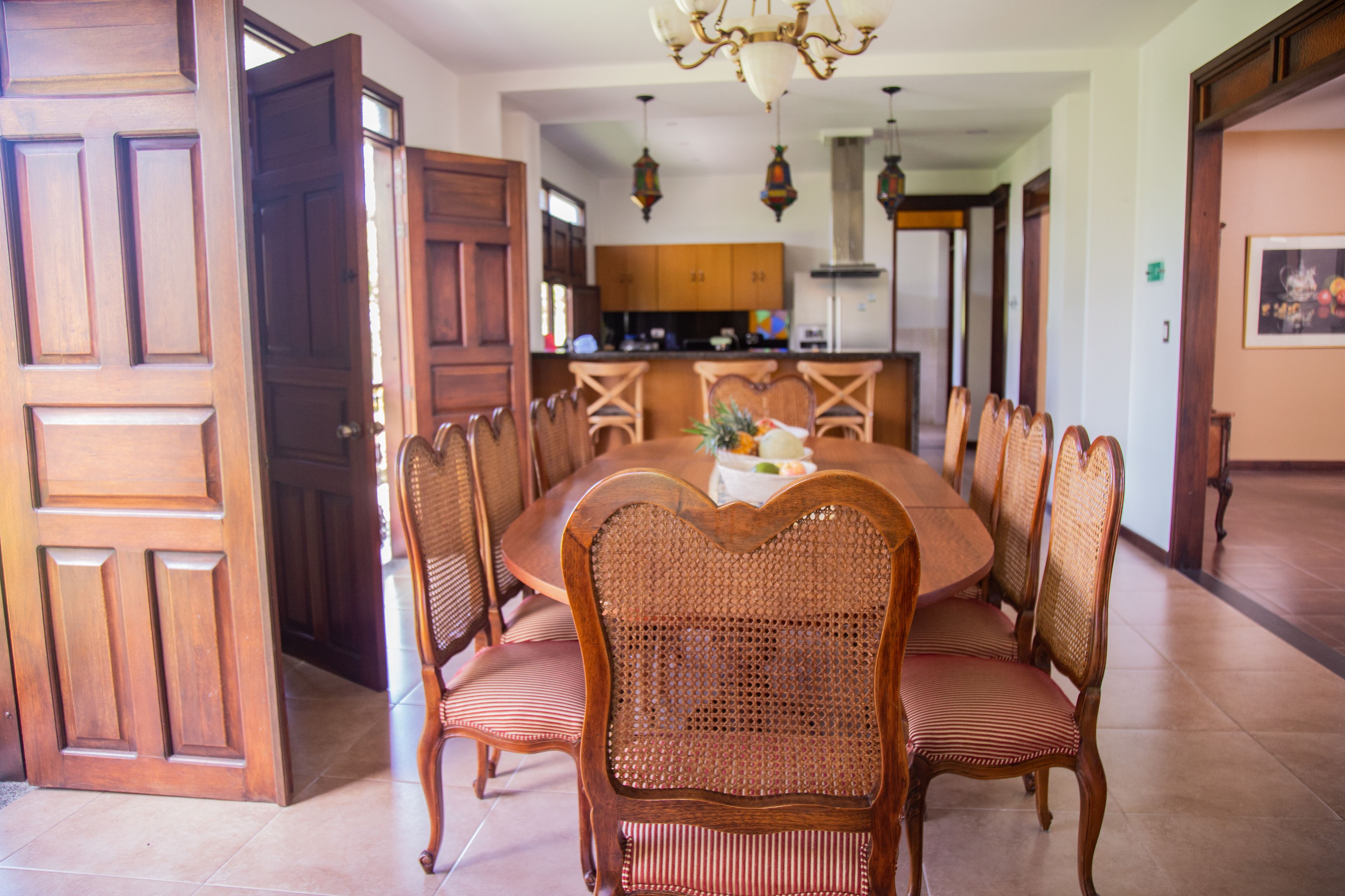 A dining area with a round table and wicker chairs, wooden cabinets, and a chandelier.