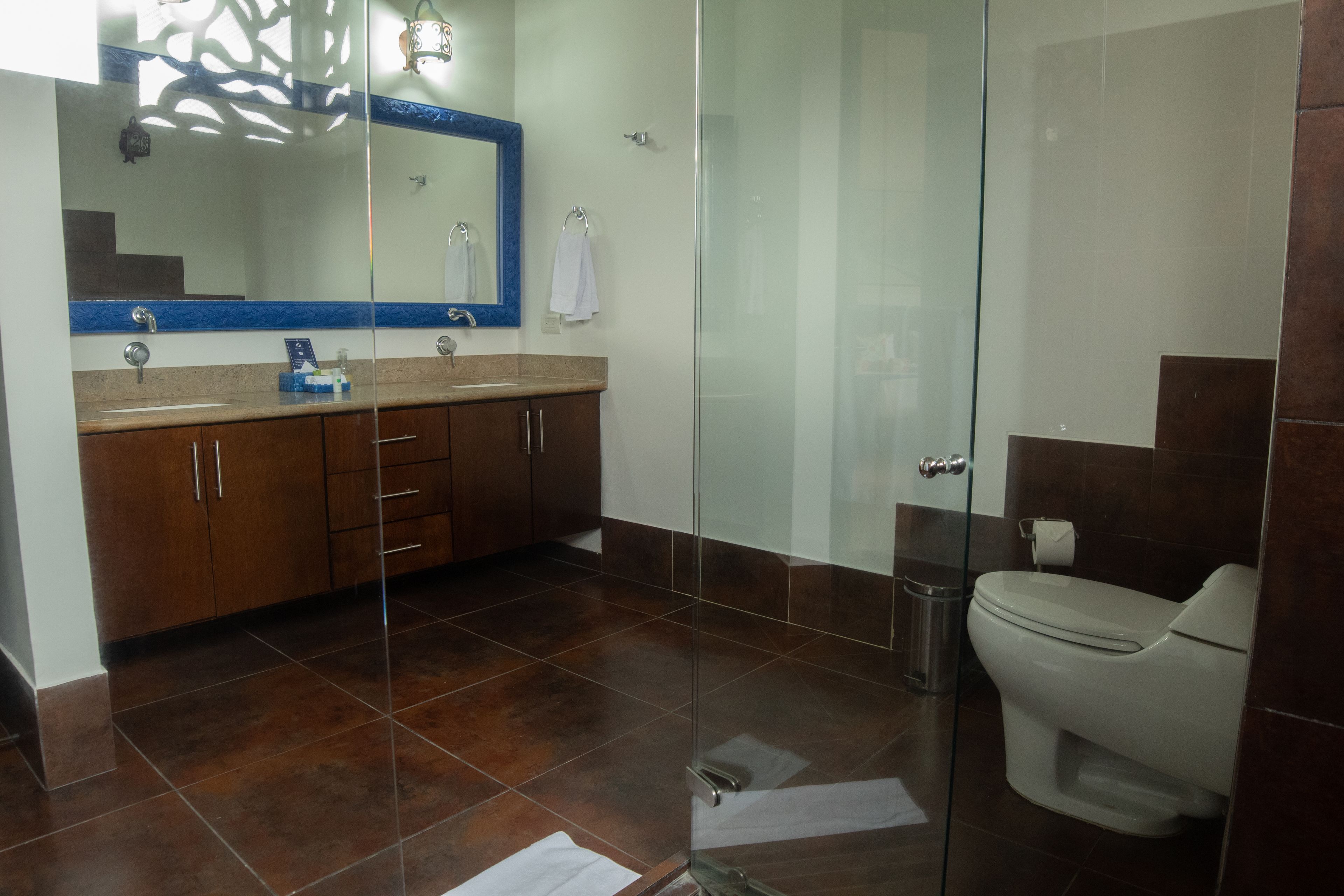 A modern bathroom with a glass shower enclosure, a white toilet, and a wooden vanity with a blue-tiled countertop.