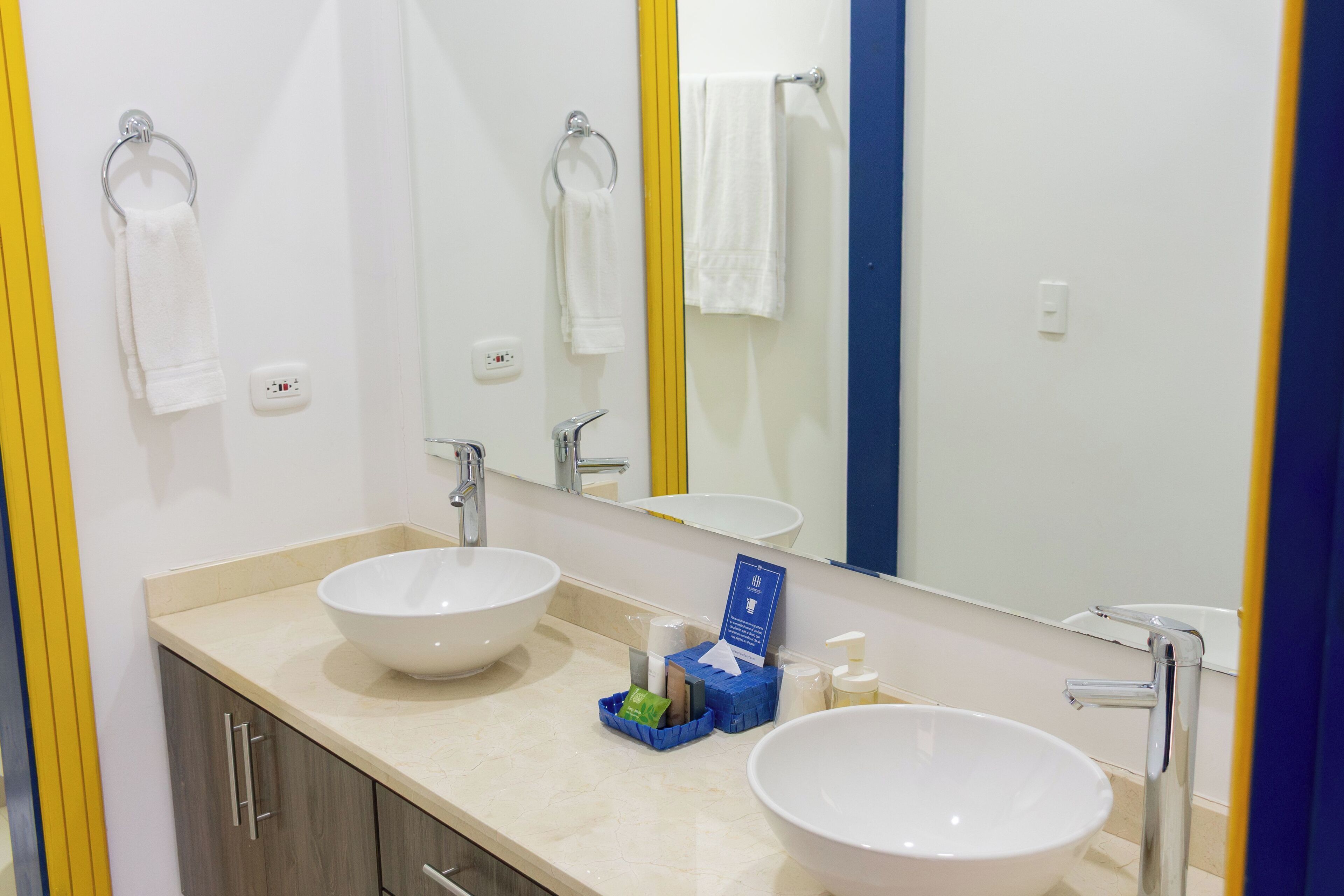 Un baño con dos lavamanos, un espejo y un perchero para toallas.