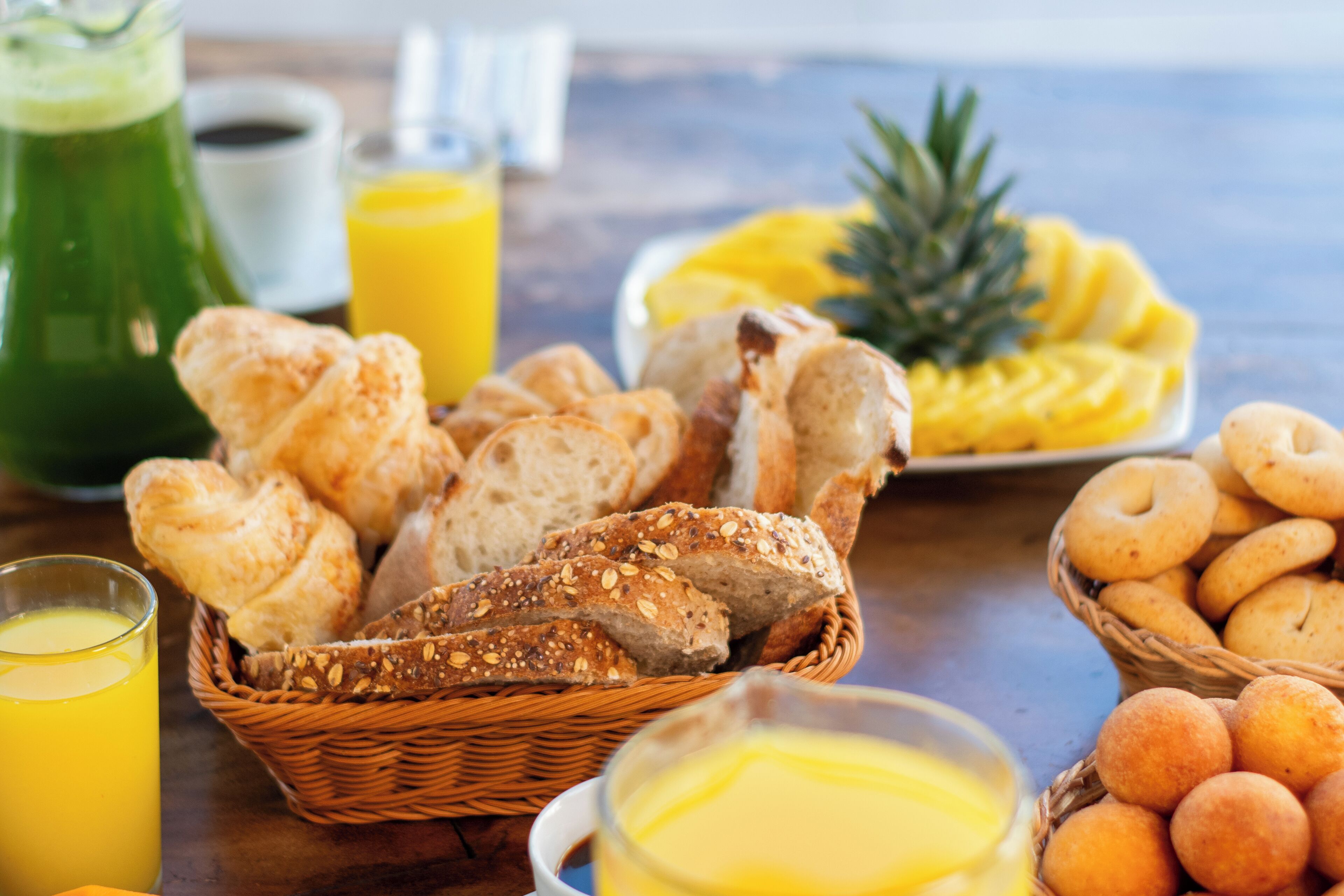 A breakfast table with bread, pastries, a pineapple, and a glass of orange juice.