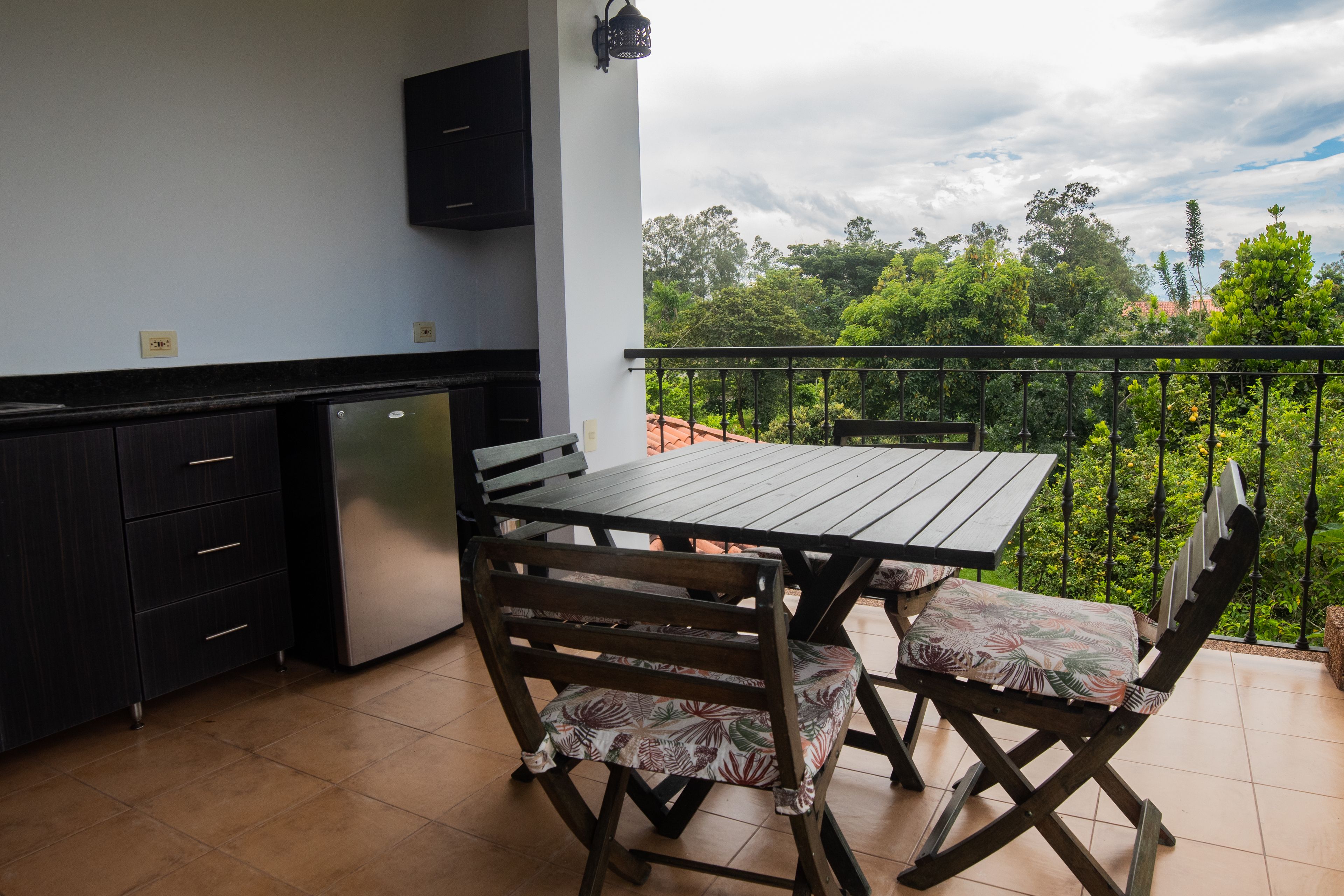 Un balcón con una mesa y sillas, una pequeña cocina y vistas a vegetación exuberante.