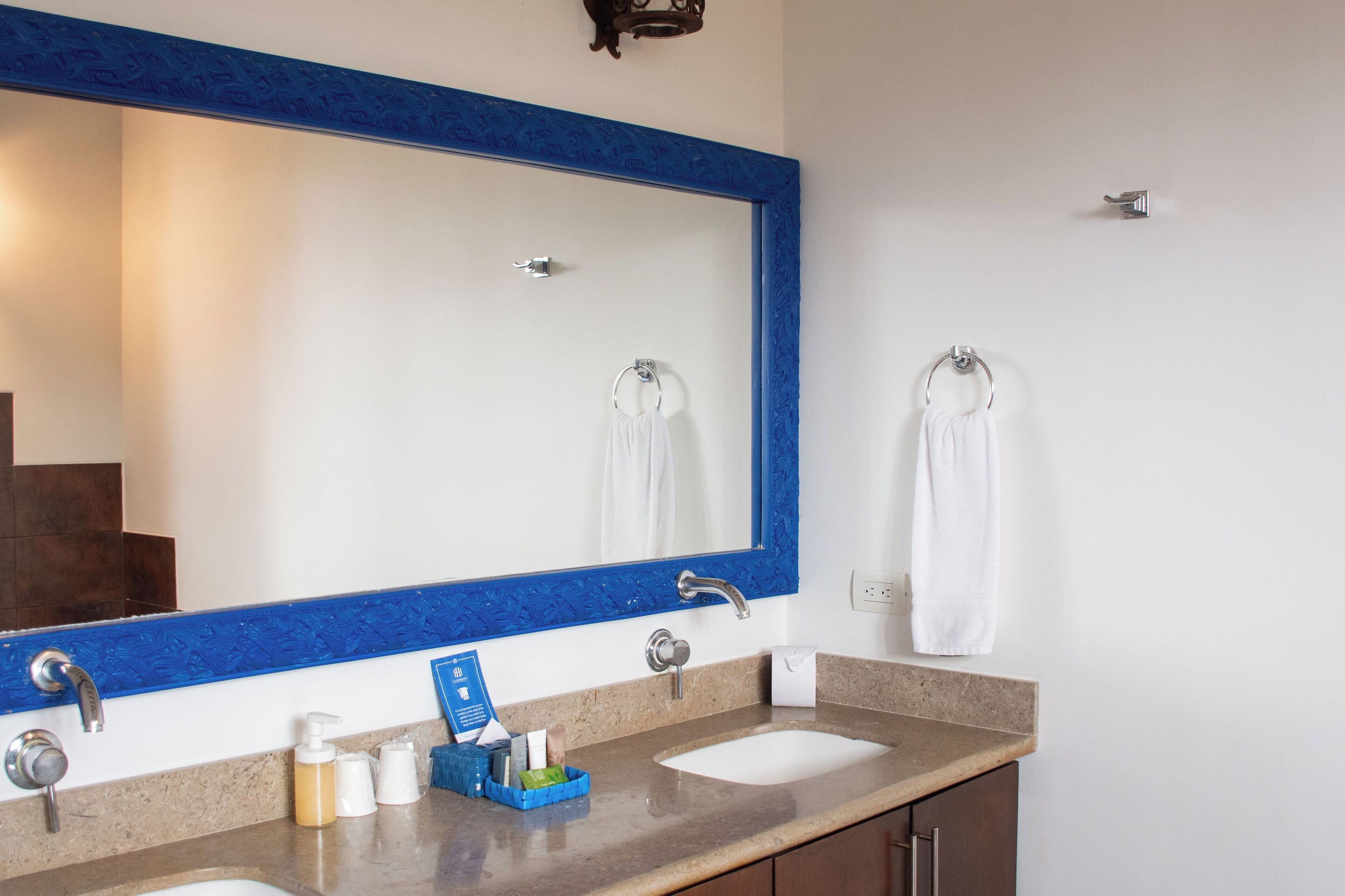 A bathroom with two sinks, a large mirror with a blue frame, and towels hanging on hooks.