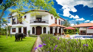 A two-story house with a balcony, a swimming pool, and a garden with purple flowers. - La Herencia Hotel (Armenia)