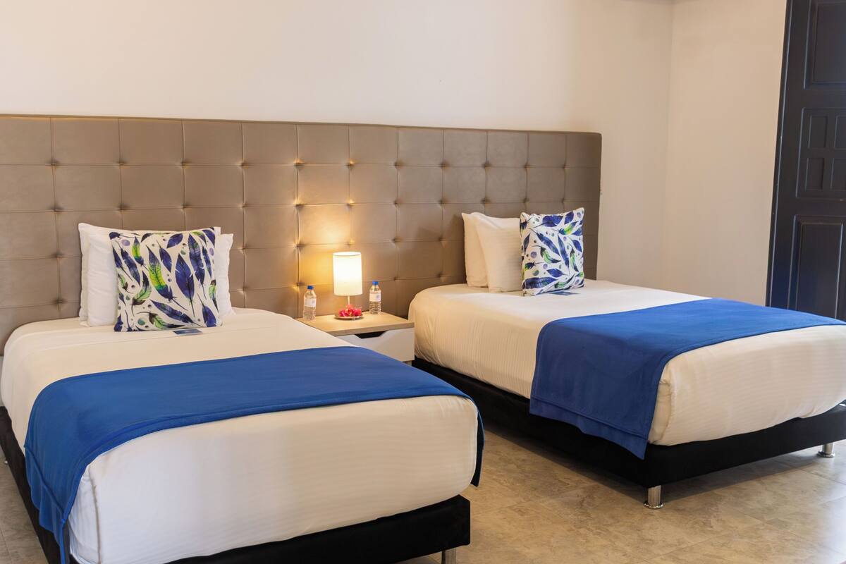 A hotel room with two beds, a tufted headboard, bedside lamps, and a nightstand with a water bottle.