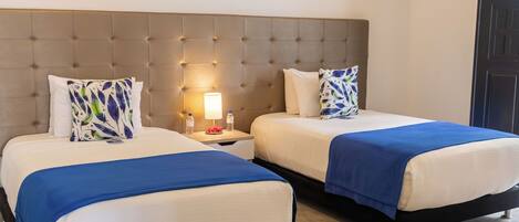 A hotel room with two beds, a tufted headboard, bedside lamps, and a nightstand with a water bottle.