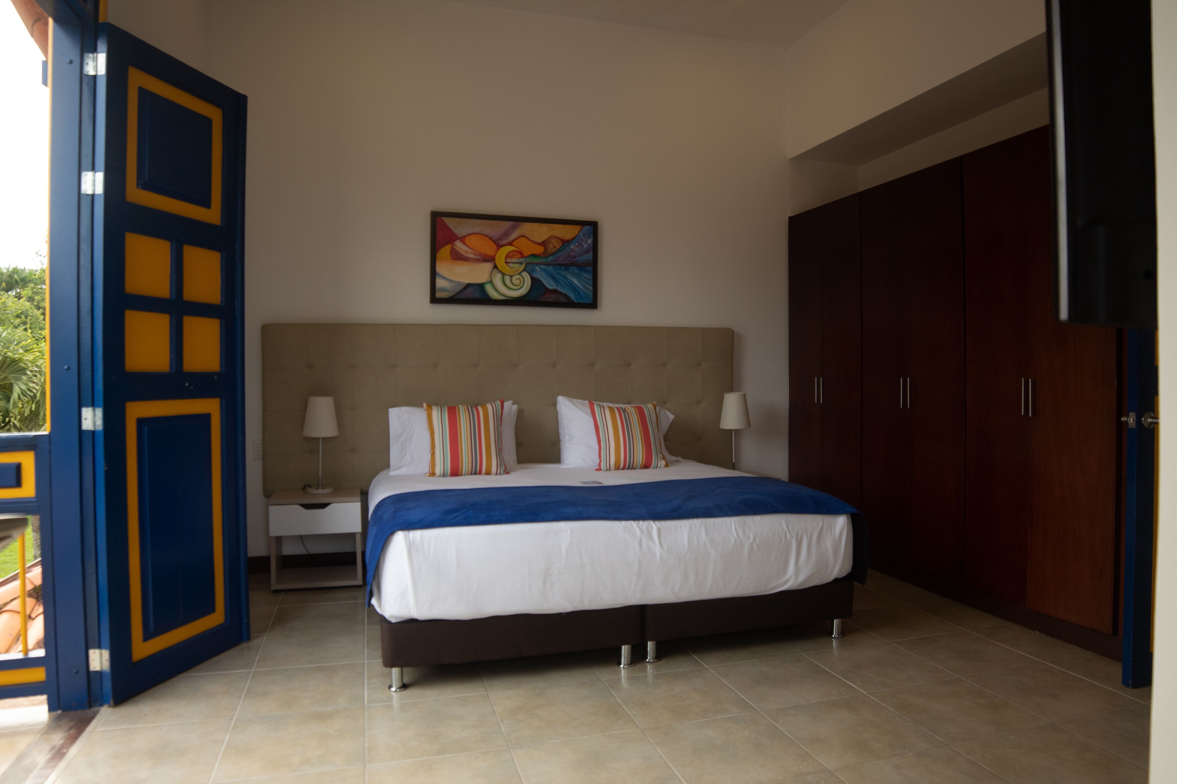 A bedroom with a bed, nightstands, a painting, and a wardrobe.