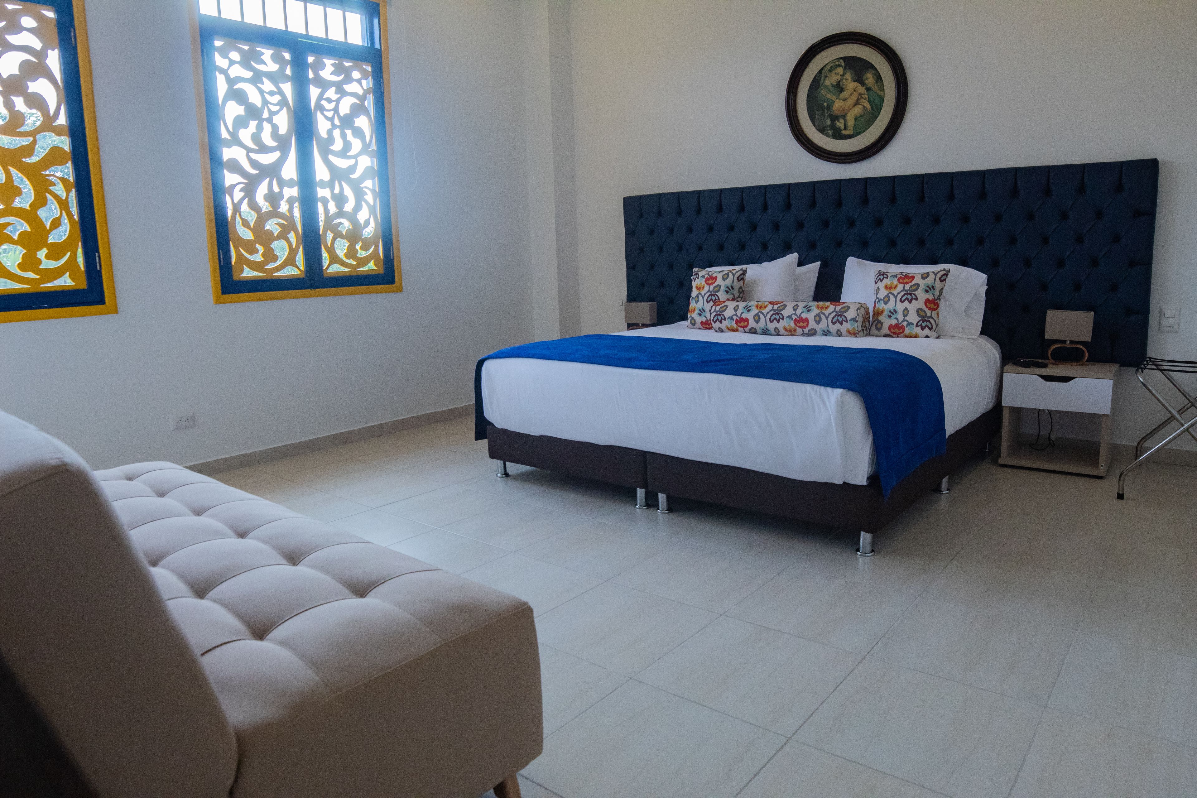A bedroom with a large bed, a nightstand, a chair, and a window with decorative glass.