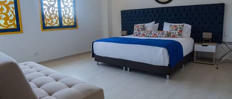 A bedroom with a large bed, a nightstand, a chair, and a window with decorative glass.