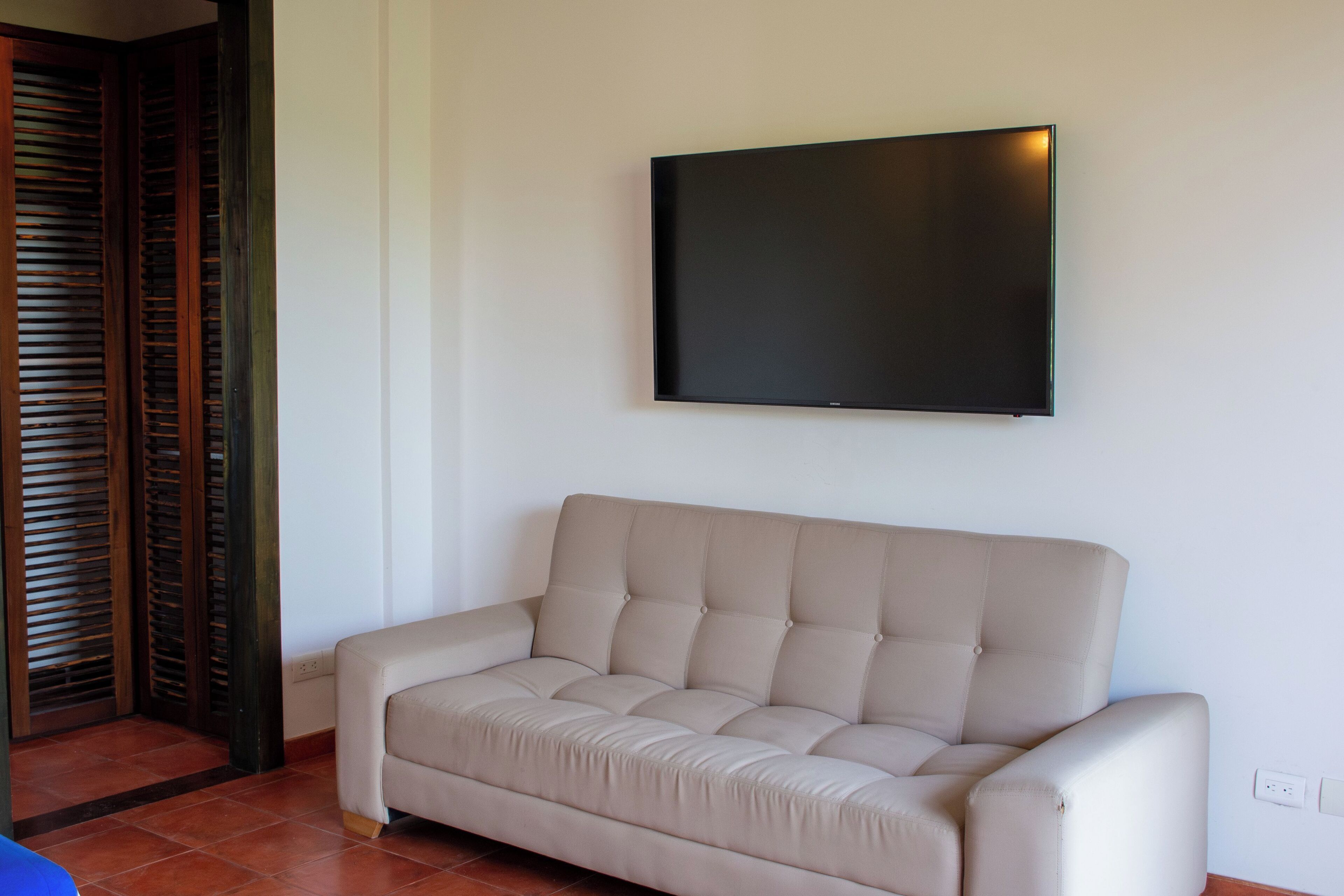 Ein beiges Sofa mit einem flachbildfernseher, der an der Wand darüber angebracht ist.