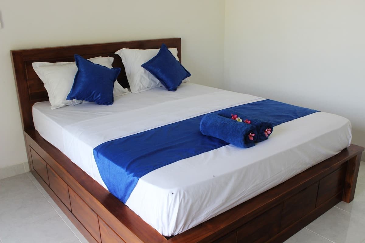Uma cama bem arrumada com cabeceira de madeira, roupa de cama branca e azul, e uma toalha azul com flores.