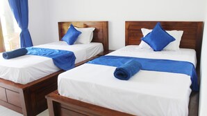 Twee eenpersoonsbedden met houten hoofdborden, wit beddengoed en blauwe accenten.