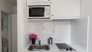 A compact kitchen with white cabinetry, a built-in microwave, a sink, and a small refrigerator. - King's Street Apartments (Zagreb)
