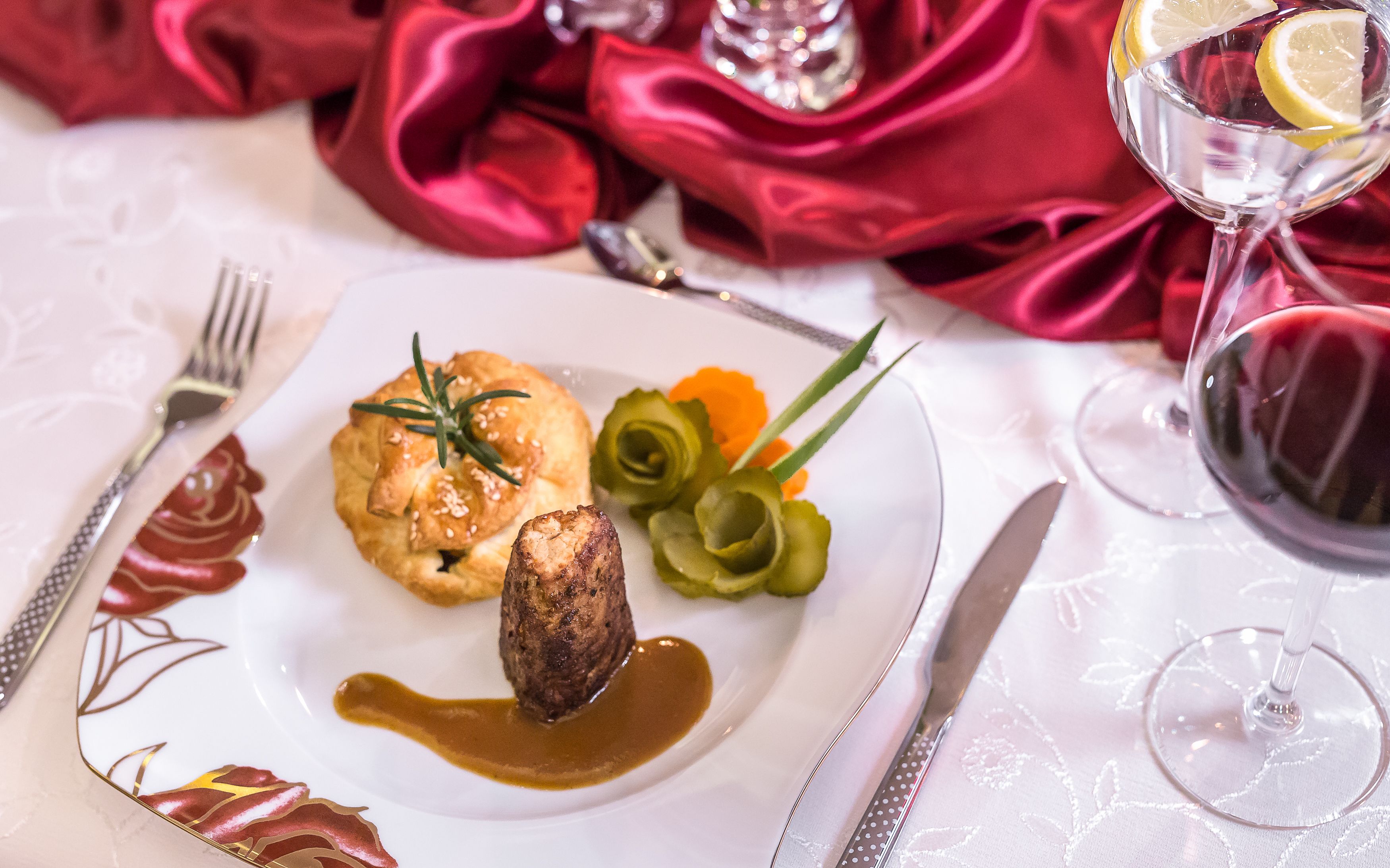 A plate with food, a glass of red wine, and cutlery on a tablecloth.